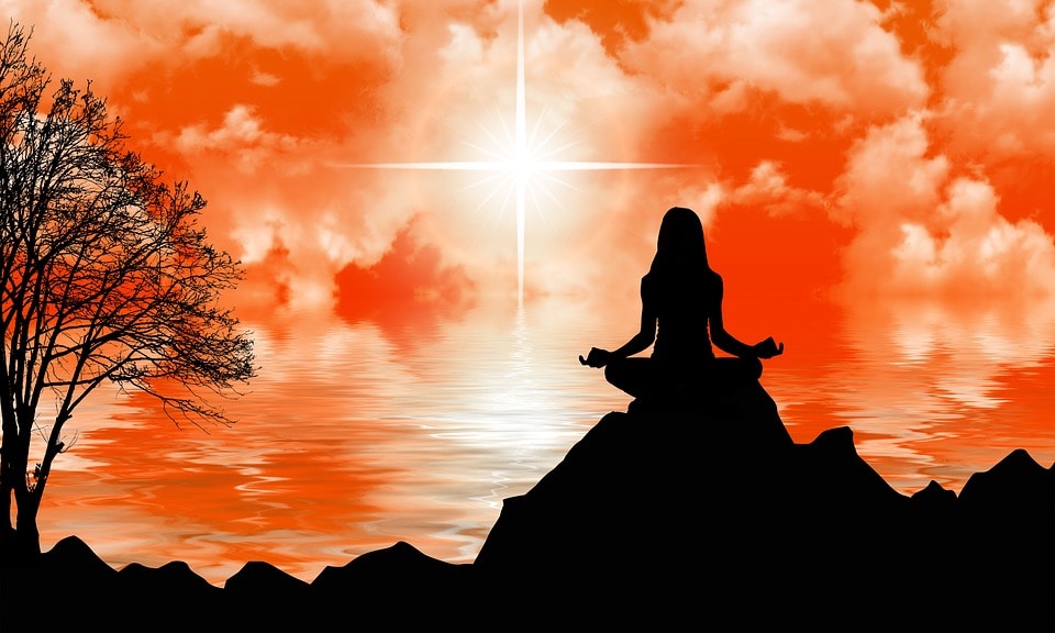 woman meditating on a mountaintop against an orange sunset
