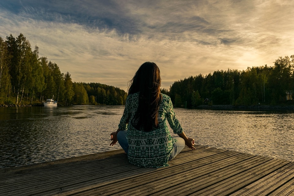 woman meditating by a lake in the forest