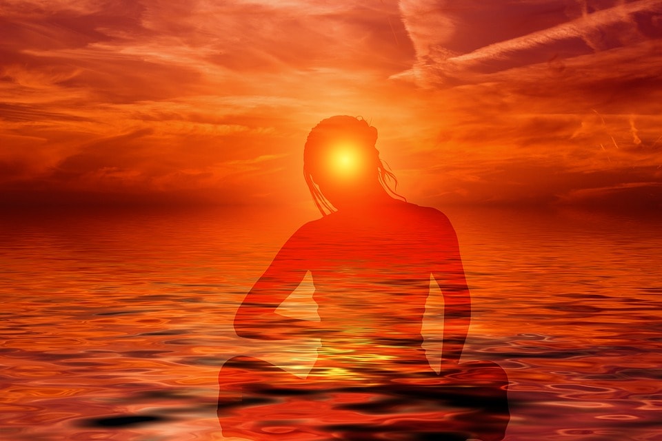 person meditating by water with an orange aura