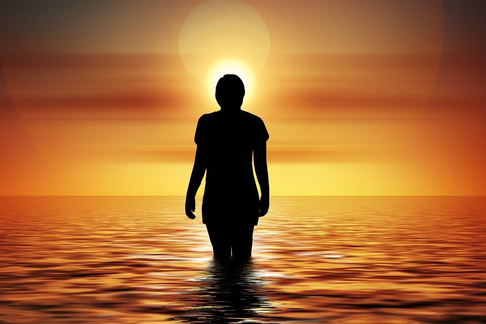 person meditating in water with an orange aura