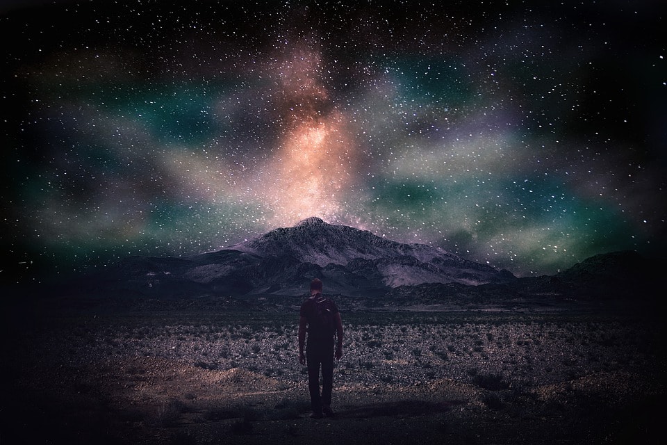 man by mountain at night with stars